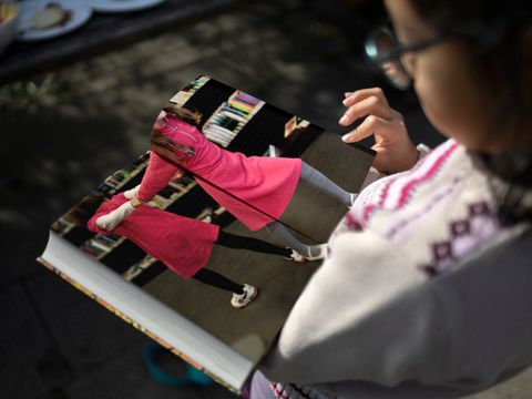 Junges Mächen schaut in Bildband, in dem ein Foto mit tanzenden Kindern zu sehen ist