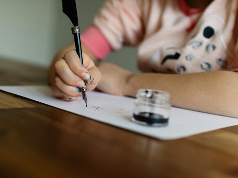 Fotografie einer Kinderhand, die mit Tintenfüller auf einem Papier schreibt