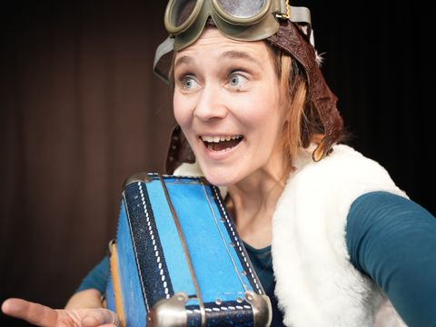 Frau mit großem Lachen, Fligermütze und einem Koffer