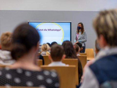 Schüler*innen sitzen vor Smartboard - Referentin mit Mund-Nasen-Schutz