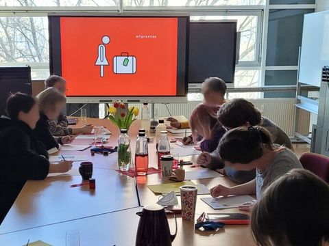 Tisch mit Menschen und Bildsdhirm mit Piktogramm