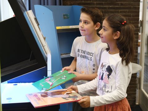 Zwei Kinder leihen Bücher am Selbstverbucher aus