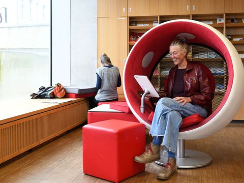 Eine Person sitzt in einem Loungesessel und schaut auf ihr Tablet