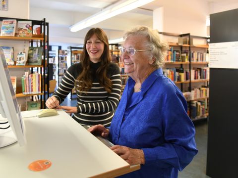 Eine Bibliothekarin berät eine ältere Dame in Sachen PC-Nutzung