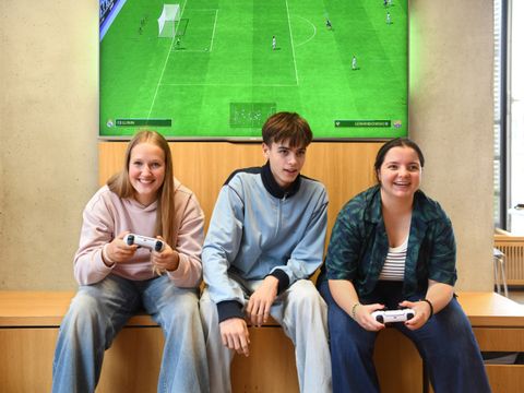 Drei junge Menschen spielen zusammen ein Konsolenspiel in der Bibliothek
