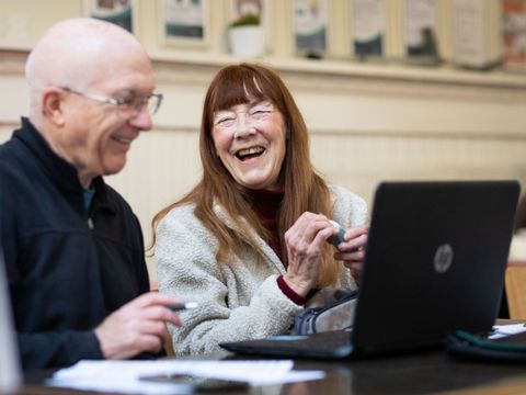 Zwei ältere Menschen arbeiten am Computer und lachen