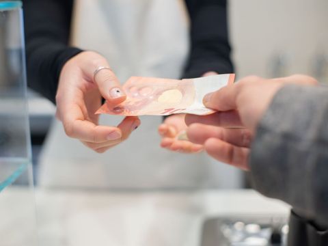 Eine Person reicht einen 10 Euro Schein zum Bezahlen