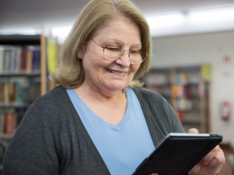 Eine ältere Frau schaut etwas auf einem Tablet in einer Bibliothek