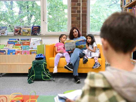 Eine Erwachsene liest Kindern auf dem Sofa vor. Ein Junge liest ein Buch.
