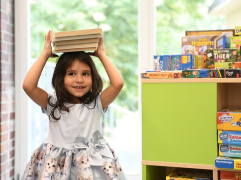 Ein Kind balanciert einen Stapel Bücher auf dem Kopf