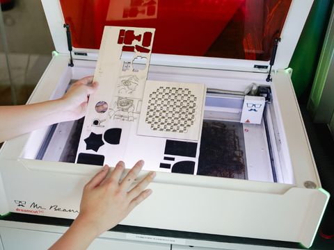 zwei Hände halten ein Stück ausgestanztes Holz im Lasercutter