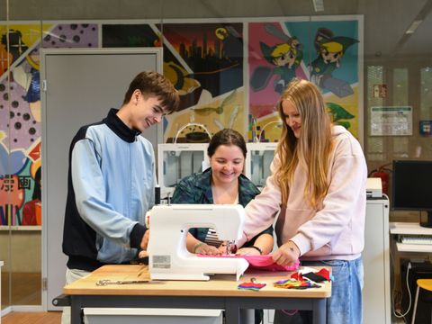Drei junge Menschen stehen lachend um eine Nähmaschine im Makerspace der Schiller-Bibliothek und setzen ein Kreativprojekt um