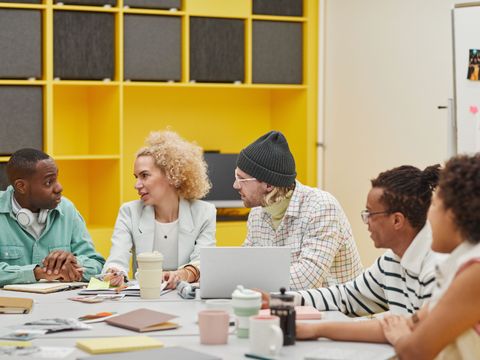 fünf Menschen unterschiendlicher Hautfarbe sitzen an einem Tisch und reden miteinander