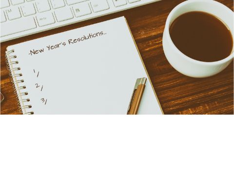 Bllick auf einen Schreibtisch mit Tastatur, Kaffeetasse und Block: New year's Resolutions