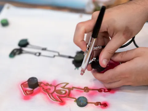 zwei Hände sprühen mit einer Airbrushpistole auf eine Vorlage