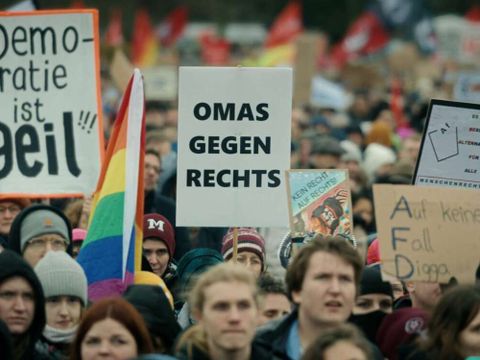 Menschenmenge bei Demonstration mit Schildern, darunter 'Demokratie ist geil', 'OMAS GEGEN RECHTS' und weitere Plakate