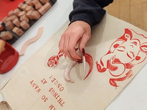 Hand mit rotem Nagellack hält einen roten Stempel über einem hellen Stoff mit rotem Elefantenmotiv und rotem Text