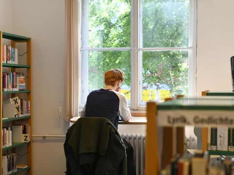 Ein junger Mann sitzt am Fenster in der Bibliothek und liest