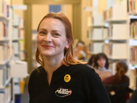 Eine Frau mit rotblondem Haar, ein freundliches Lächeln. Sie trägt eine Jacke mit dem Logo der Bibliothek.