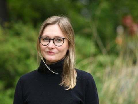 Eine Frau mit dunkelblonde Haare und eine große Brille lächelt sanft.