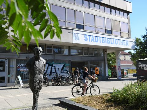 Das Gebäude der Heinrich-Böll-Bibliothek von außen. Ein Skulptur des Autors Heinrich Böll steht vor der Bibliothek.