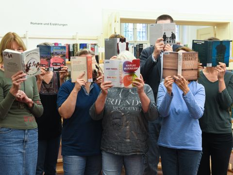 Team der Bibliothek. Alle verstecken ihre Gesichter hinter Büchern.