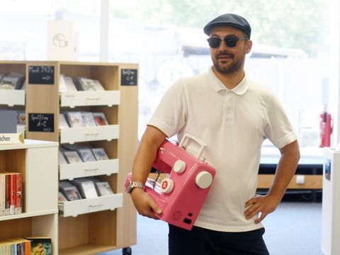 Ein Mann hält eine pinke Nähmaschine in einer Bibliothek
