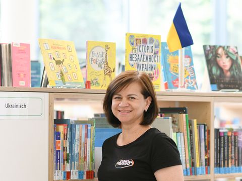 Bibliothekarin steht vor einem Regal mit ukrainischsprachigen Bücher und einer Ukrainefahne