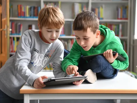 Zwei Kinder in Grundschulalter arbeiten mit Tablets in einer Bibliothek.