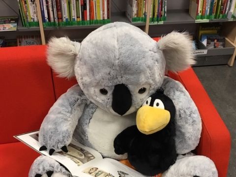 zwei Kuscheltiere mit Buch sitzen auf dem Sofa