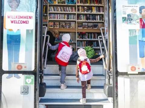 Zwei Kinder betreten den Bücherbus mit Rucksäcken
