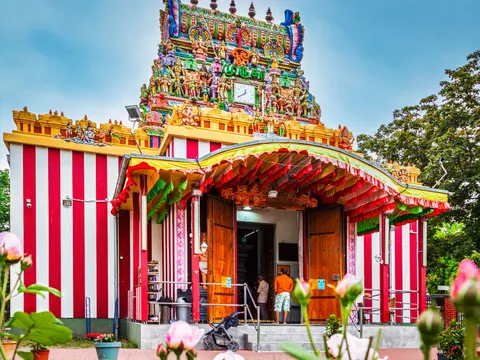 Ein Hindutempel. Der unterer Teil des Tempels ist rot-weiß gestreift gestrichen. Darüber eine Art Turm mit vielen hinduistischen Göttern. Die Götter sind sehr farbenfroh angemalt.