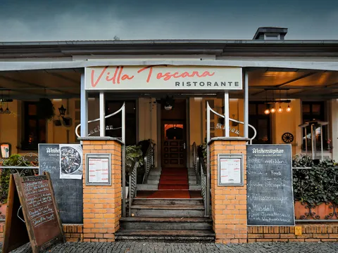 Eingansbereich zum Restaurant. Rechts und links des Eingangs zwei gemauerte Stelen. Oben eine Markise mit der Aufschrift "Villa Toscana"
