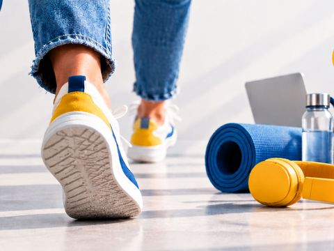 Person in Sportschuhen beim Gehen, daneben liegen eine Fitnessmatte, Hanteln und eine Trinkflasche.