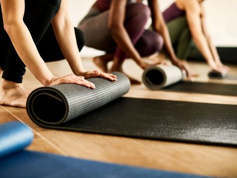 Mehrere Personen rollen in einem Fitnessstudio ihre Yogamatten auf dem Holzboden aus.