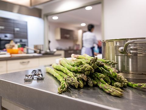 Grüner Spargel liegt auf dem Edelstahl-Küchentisch neben Topf und Spargelschäler