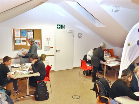 Mehrere Personen sitzen an Tischen in einem Raum und lernen
