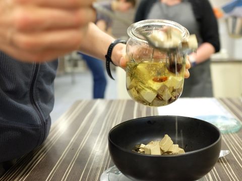 Aus einem Glas mit eingelegten veganen Käsewürfeln wird eine Portion entnommen mit einem Löffeln