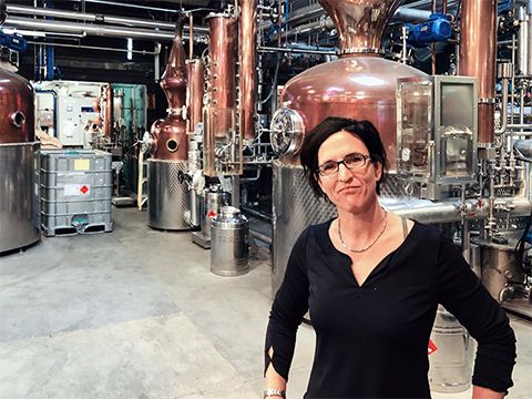 Kursleiterin Tanja Bempreiksz in einer Londoner Brennerei vor kupferfarbenen Tanks