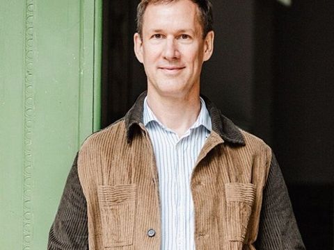 Portrait-Dr.-Ralf-Müller: Er steht angelehnt an einer Holztür