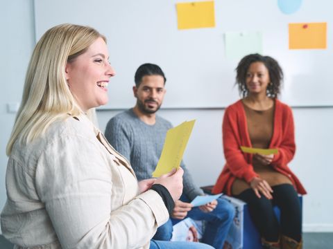 Gesprächsrunde mit drei Leuten, eine lächelnde Frau hält eine Moderationskarte hoch