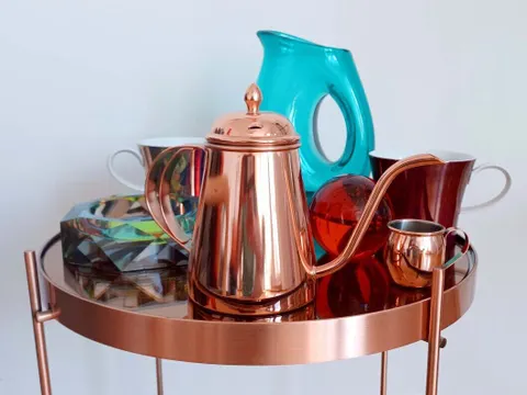 Kupfertisch mit schönen Tassen, einem Kaffeekännchen, einer Karaffe und roter Kugel