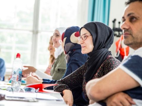 Fünf Personen sitzen gemeinsam am Tisch im Unterricht: drei Frauen mit Kopftuch, eine Frau ohne Kopftuch und ein Mann