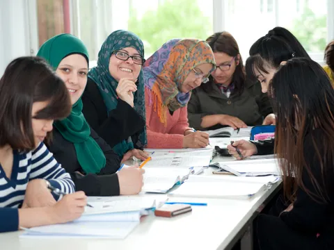 Sieben Frauen sitzen an einem Tisch, davon drei mit Kopftuch, und lernen gemeinsam