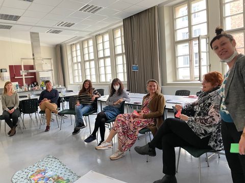 Mehrere Personen sitzen in einem Stuhlkreis in einem hellen Raum, eine Frau vorne erklärt.
