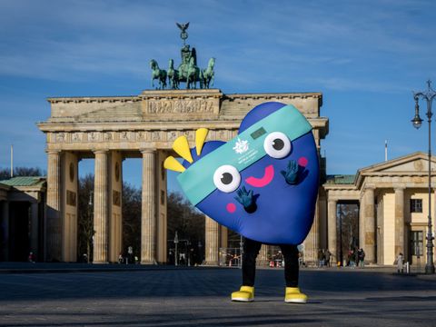 Blaues Maskottchen steht vor dem Brandenburger Tor