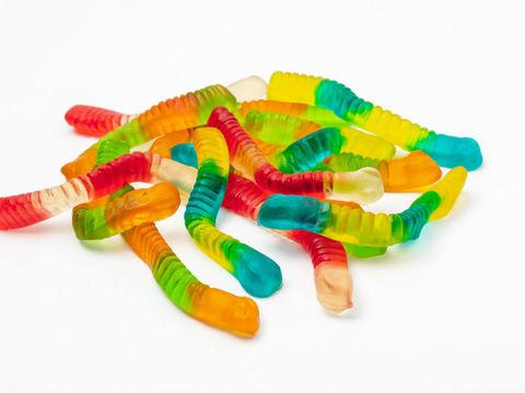 Bunte Gummiwürmer liegen auf einer weißen Fläche.