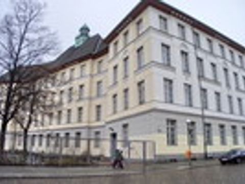 Ein mehrstöckiges Schulgebäude mit weißen Fassaden und grünen Dächern vor kahlen Bäumen.