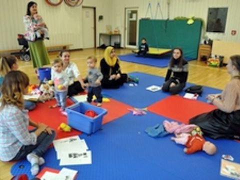 Kinder und Erwachsene sitzen gemeinsam auf Matten in einem Raum mit Lernmaterialien
