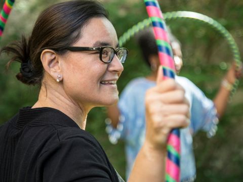 Nahaufnahme einer lachenden Frau mit Brille, die einen bunten Hula-Hoop-Reifen in der Hand hält